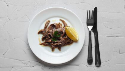 Plate with canned anchovy fillets and lemon wedge on white textured table, top view