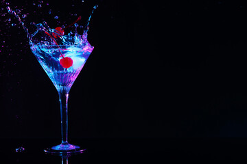 Adding cherries into glass with martini on black background, space for text