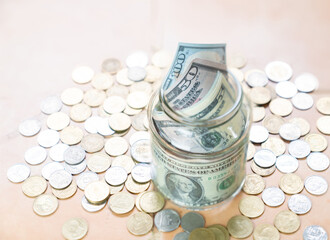 Dollar bills and coin in glass jar on the table.