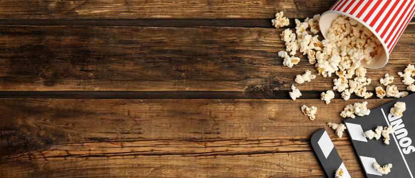 Tasty popcorn and clapboard on wooden table, flat lay with space for text. Banner design