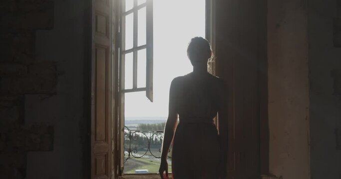 Silhouette of female walking away from castle window with bright sunshine, front view