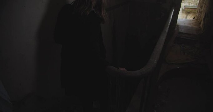 Woman walk down into darkness on old abandoned staircase, back view