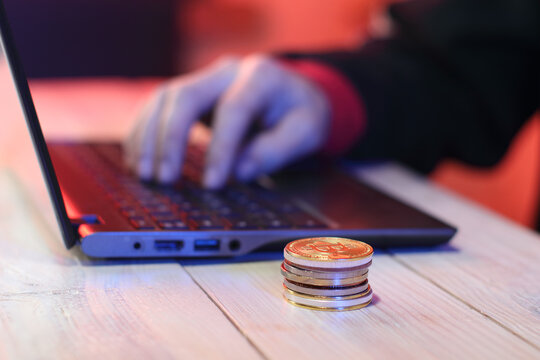 a pile of coins on a table next to a laptop and a person's hand