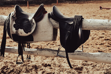 Horse saddles and bridles standing on fence at horse farm riding arena