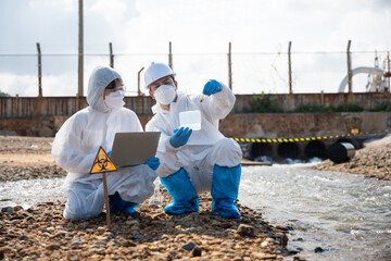 Ecologist sampling taken dead fish to inspaction and save data to laptop computer, Biologist wear protective suit and mask collects sample of waste water from industry, problem environment