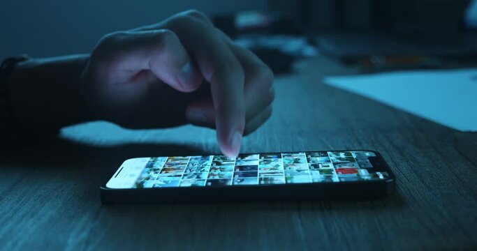Close-up of male's hand scrolling social media in the smartphone at night time. Man Browse Social Network. Touch with Fingers the display of Mobile Phone.