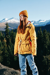 Young woman full-length hiker in yellow raincoat running and walking on a mountain trip in the fall and hiking in the mountains at sunset freedom