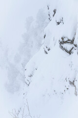 Steep mountain slope in the shape of a huge monkey head in a snowstorm and fog