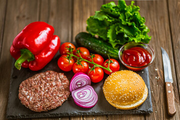 High angle view of ingredients for classic beef burger on stone board with knife. Selective focus. 