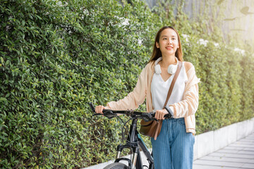 Fototapeta na wymiar Happy female smiling walk down the street with her bike on city road, ECO environment, healthy holiday travel, Asian young woman walking alongside with bicycle on summer in park countryside outdoor