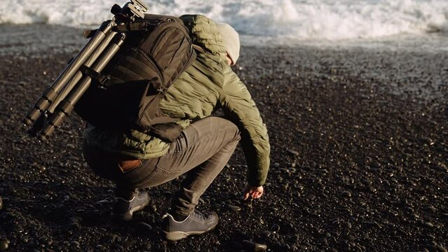 Man crouching for pebble on black beach