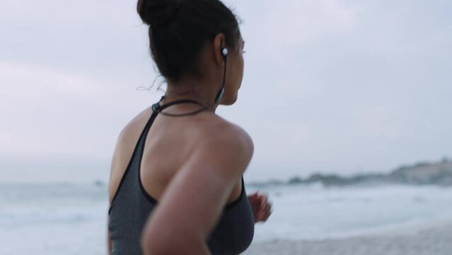 Beach running, woman and headphones of a runner by the ocean doing exercise with music. Back view of marathon training, sports and fitness workout by the Florida sea for wellness in nature with audio