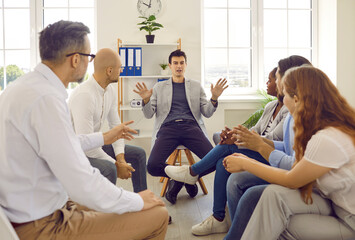 Business team talking during a work meeting in the office. Group of people sitting and listening to a young man who is speaking, explaining something and gesticulating