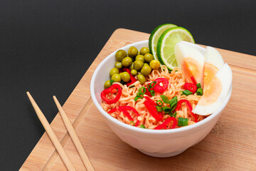 Beautiful Noodle Dish with Green Pea, Eggs, Red Hot Pepper, Greens and Lime with Chopsticks on Bamboo Cutting Board. Instant Noodles