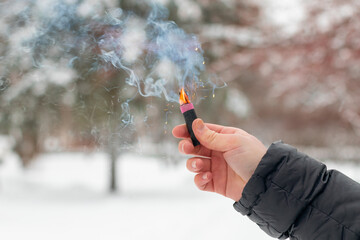 Burning Firecracker in a Hand. Guy Holding a Petard Outdoors in Winter at Daytime. Loud and Dangerous New Year's Entertainment. Hooliganism with Pyrotechnics. Noise of Firecrackers in Public Places