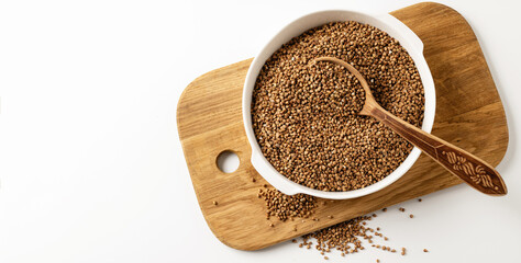 Dry uncooked buckwheat groats in white dish, wooden board, spoon, on white background, banner, top...