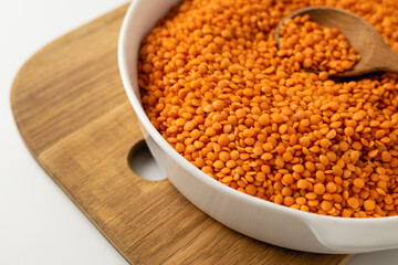 Dry uncooked red lentil groats in a white dish, wooden board, spoon, on a white background, close-up