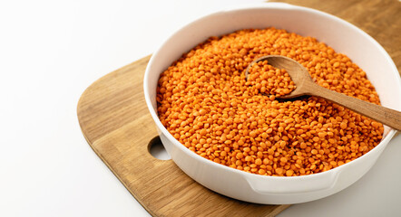 Dry uncooked red lentil groats in a white dish, wooden board, spoon, on a white background, close-up