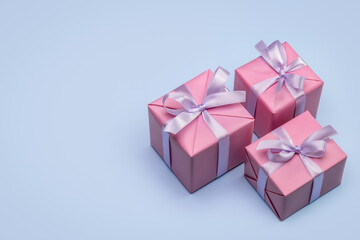 Three stylish gift boxes wrapped in pink paper, decorated with satin ribbon and bows. Studio shot, blue background, copy space.