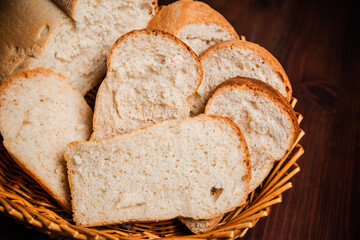 Sliced loaf of bread in a wicker basket on a wooden brown background