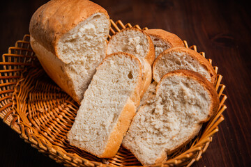 Sliced loaf of bread in a wicker basket on a wooden brown background