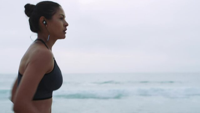 Woman, running and beach music at sunset with earphones for athlete marathon training in Brazil. Exercise, fitness and focus of runner girl at ocean for competition practice with audio streaming.