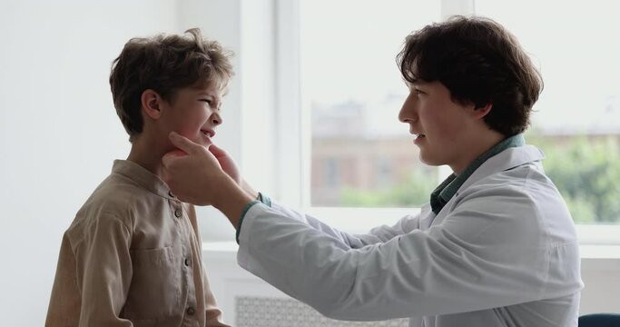 Little patient with symptoms of tonsils gets professional medical care from ENT doctor, otolaryngologist touch neck of small boy at visit in clinic. Laryngology, healthcare, otolaryngology, medicine
