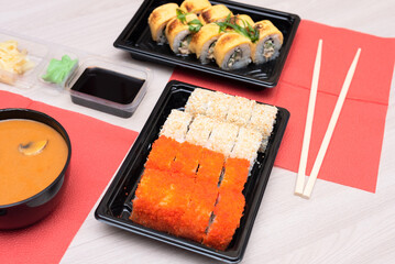 Delicious Japanese rolls with salmon, avocado, cucumber, cheese, tom yum soup in takeout packaging with wood sticks and soy sauce. Selective focus. Asian food and delivery concept. Healthy eating
