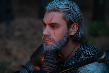 Age male warrior in chain mail with gray hair and a scar on his face at dusk. A knight in armor...
