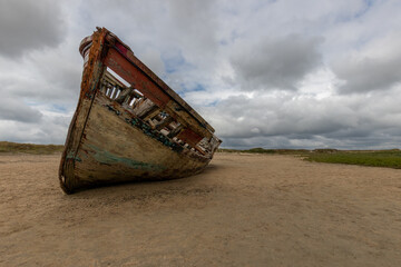 A closeup shot of an old broken boat on the coast against a cloudy sky