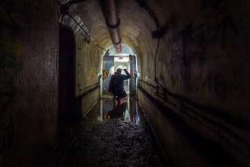 Fototapeta na wymiar Man exploring an old World War II bunker with flashlight. Dark corridor and an old steel door.