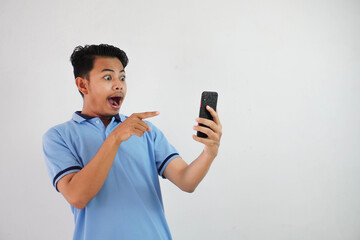portrait asian man shocked holding phone and pointing at the phone with a finger wearing blue polo...