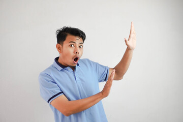 young asian man acting like he's holding side something heavy, but it's just empty copy space wearing blue t shirt isolated on white background. shocked face