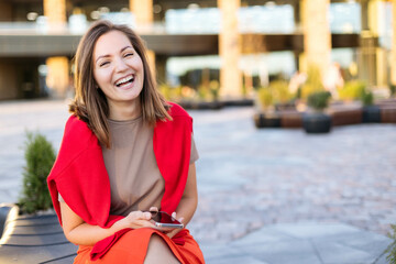 Close-up portrait of a young woman laughing happily, outdoors against the backdrop of city buildings