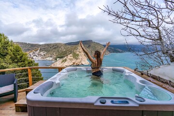 Outdoor jacuzzi with mountain and sea views. A woman in a black swimsuit is relaxing in the hotel...