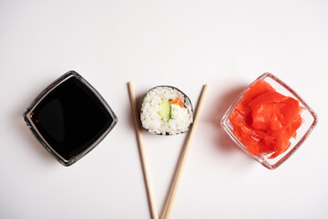 Sushi with chopsticks, soy sauce and pink ginger on a white background.