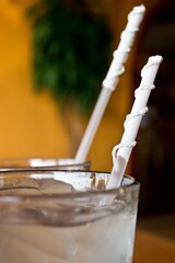 Glasses of ice water with straws with their paper wrapper twisted around.