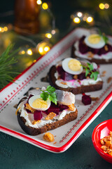 Open sandwiches smorrebroda on rye bread with marinated beetroot, cream cheese, herring and quail egg in Christmas style on a green concrete background. Sandwich recipes.
