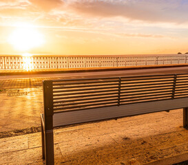 Obraz premium modern metallic bench on sea embarkment with asphalt road and beautiful seashore landscape with amazing cloudy sky