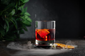 Smoked old-fashioned rum cocktail with ice cubes, lemon and flowers. Alcoholic cocktail in a glass
