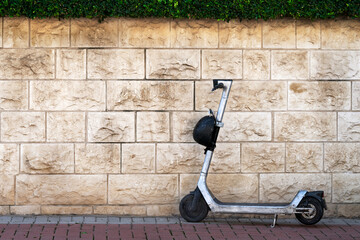 Electric scooter with a helmet stands near a stone wall on the sidewalk in Israel