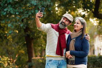 Indian old couple taking selfie in smartphone at park - Powered by Adobe