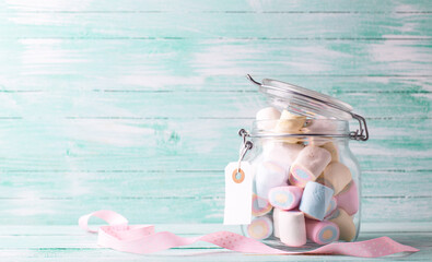 Postcard with glass jar full of colorful sweet marshmallows with emty tag on turquoise wooden background. Place for text. St. Valentines day, Mothers day concept.. - 554425617