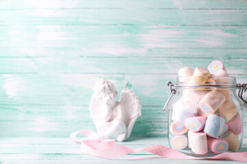 Card with glass jar full of colorful sweet marshmallows and little white angel on turquoise wooden background. Place for text. St. Valentines day, Mothers day postcard.