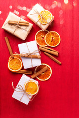 Composition from wrapped boxes with presents decorated cinnamon,  slices dried oranges on  red textured  paper background.  Natural, ogranic materials. Place for text. Top view. - 554425693