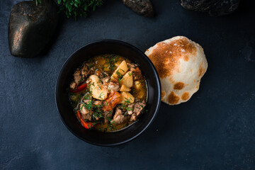 Hot stewed pork with potatoes, sweet peppers, onions in tomato sauce with herbs and flatbread in a bowl.