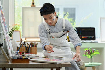 Handsome male painter creates pictures, drawing with paints on canvas in art studio. Leisure...