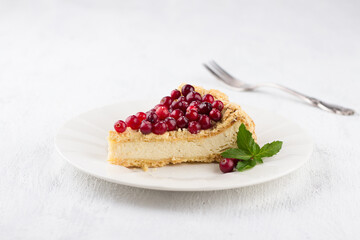 A piece of curd royal cheesecake on a white plate decorated with cranberries, mint and sprinkled with powdered sugar on a light gray background © olepeshkina