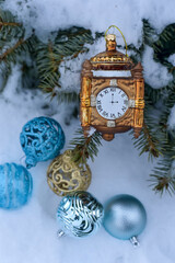 Golden Christmas clock on a branch and blue Christmas balls on the snow. New Year Christmas.