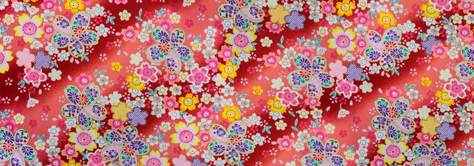 Banner depicting a detailed photograph of a Japanese pattern design illustrated with colorful flowers enhanced with golden color printed on a furoshiki cloth made in cotton fabric on a red background.